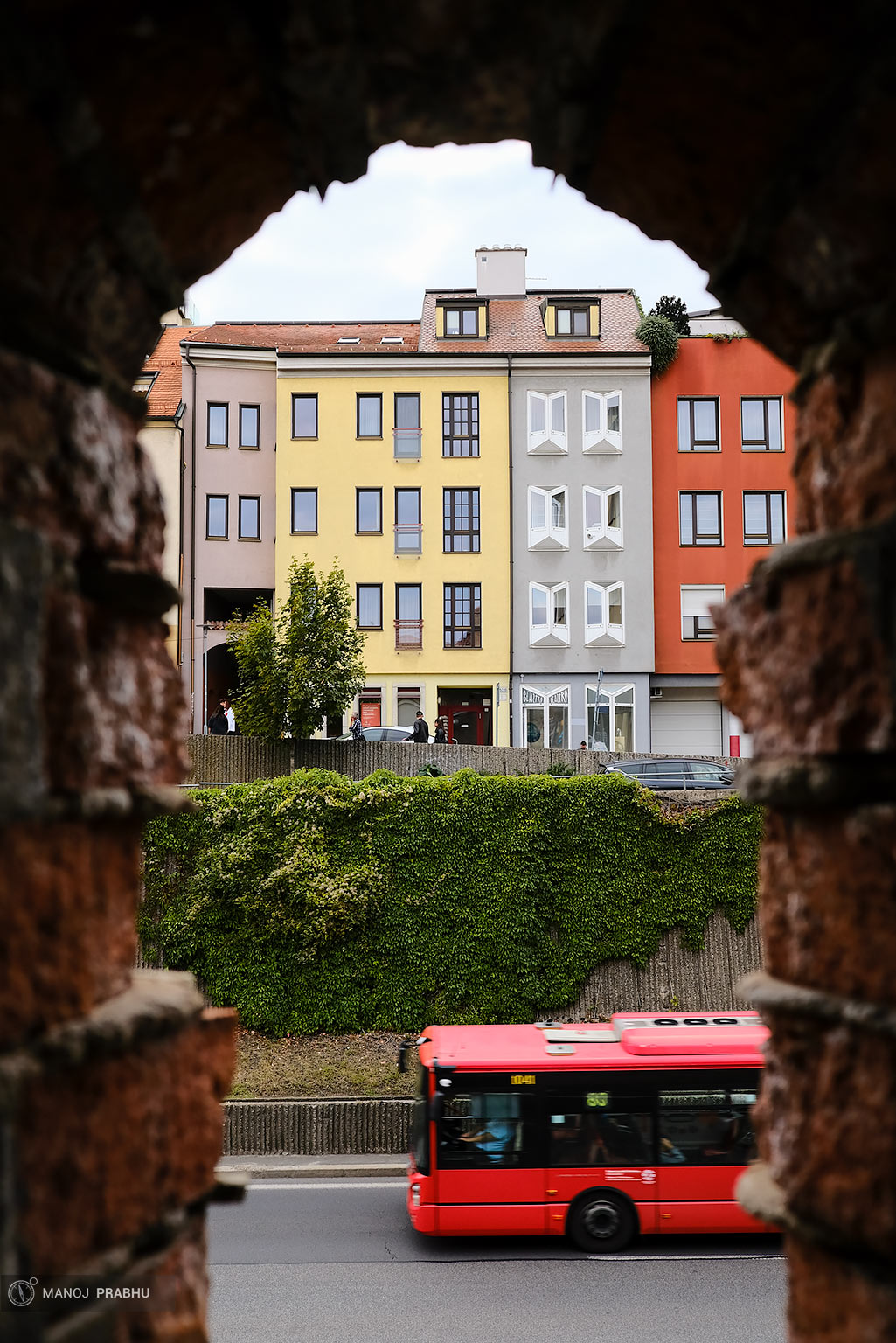 A red bus traveling in front of some colorful buildings. (Shot on Fujifilm X-Pro2 using Kodak Ektar 100 film simulation recipe)