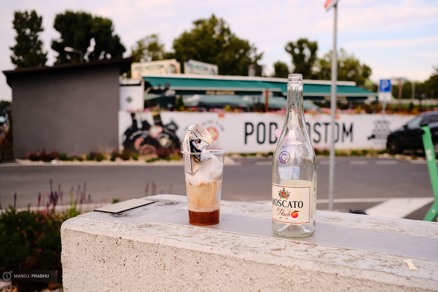 Empty wine bottle kept on wall along with a used plastic cup. (Shot on Fujifilm X-Pro2 using Kodak Ektar 100 film simulation recipe)