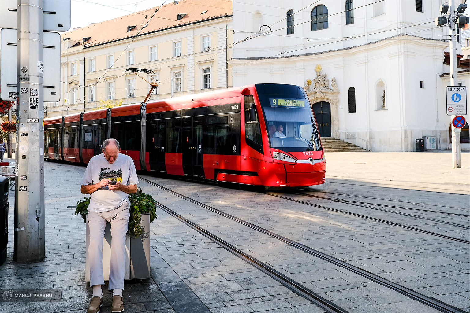 An old man peering at his phone while a tram passes behind him. (Shot on Fujifilm X-Pro2 using Kodak Ektar 100 film simulation recipe)