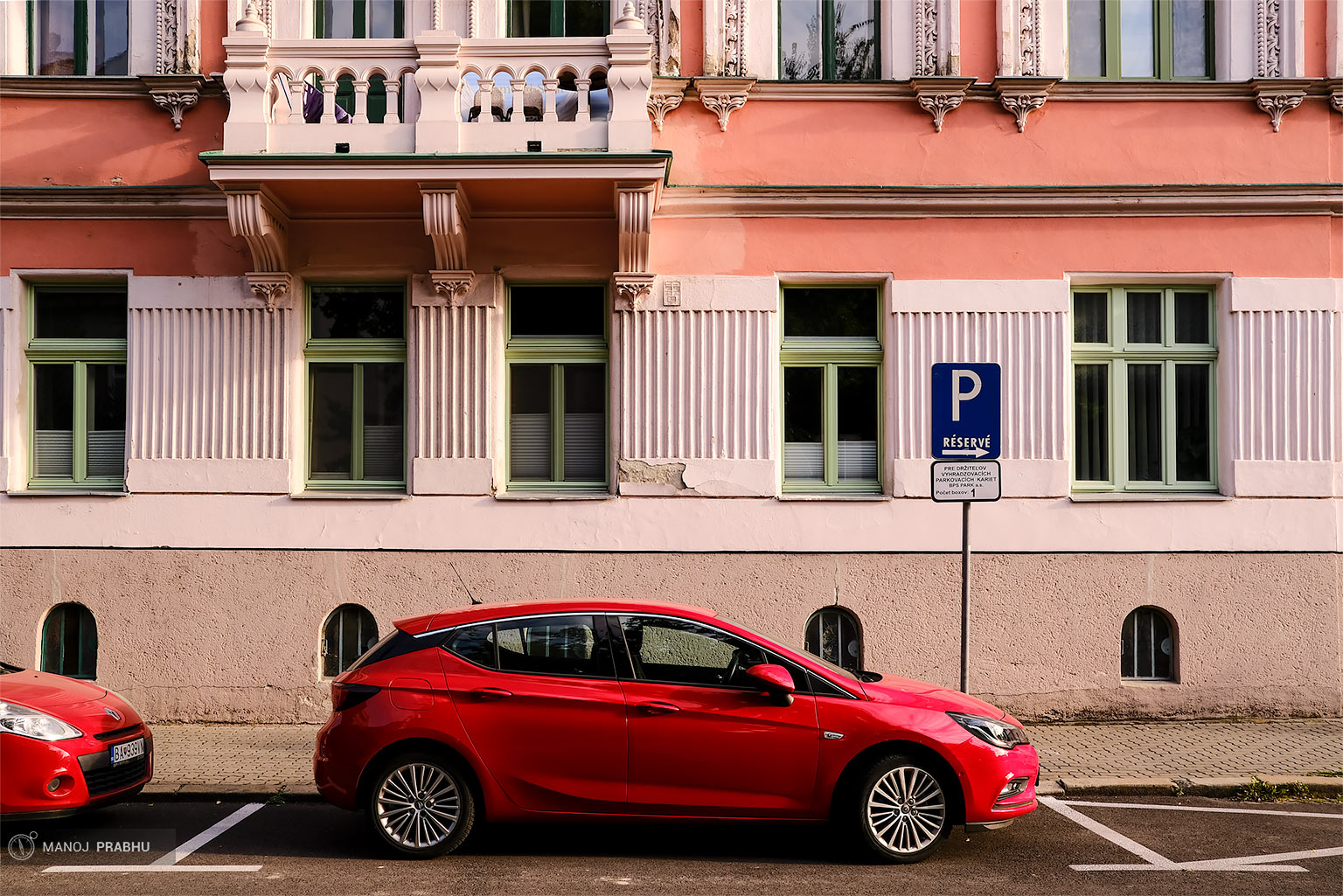 A red car parked in front of a building painted in shades of red and pink. (Shot on Fujifilm X-Pro2 using Kodak Ektar 100 film simulation recipe)